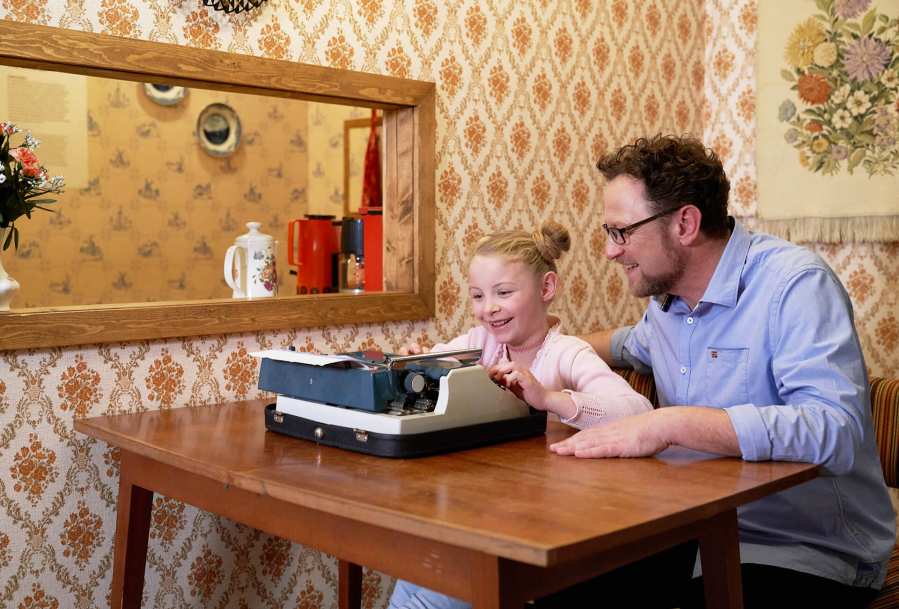Father and daughter sitting on a desk with typewriter at the DDR Museum